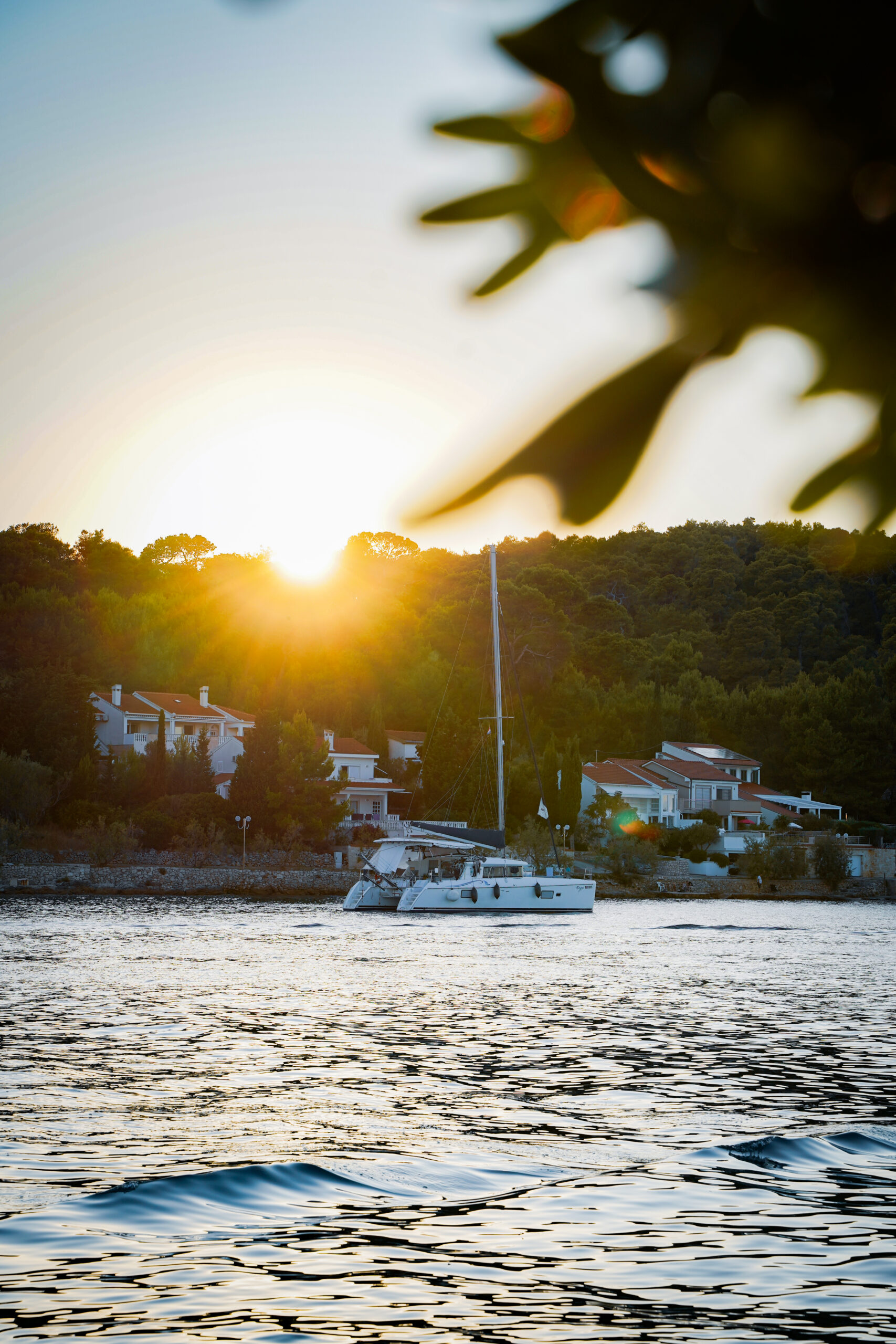 Catamaran Eragon at sunset in front of a small harbour village